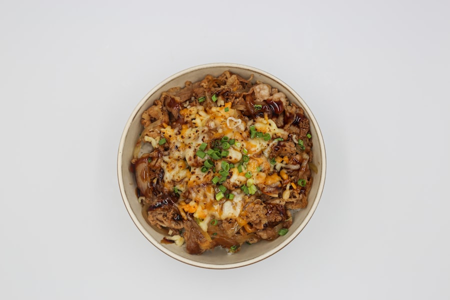 An overhead bowl of rice under seared chicken, melted cheese and sliced scallions