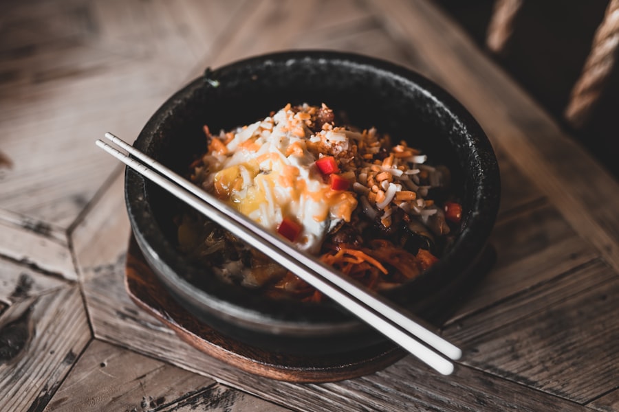 A dark bowl of rice topped with a fried egg, shredded vegetables and chilli sauce, chopsticks resting across it